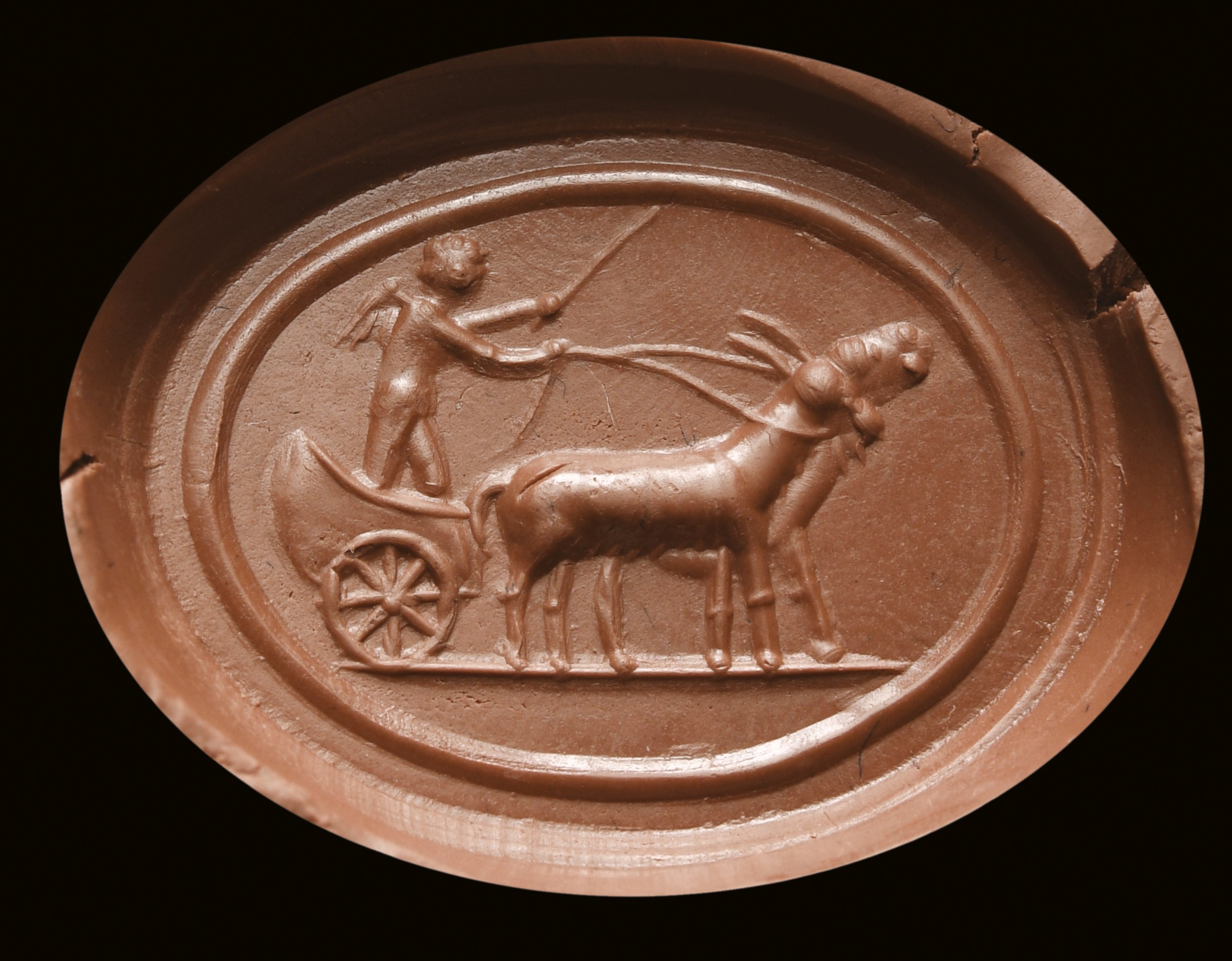A partially burnt agate intaglio. Erote on a chariot drawn by two goats.