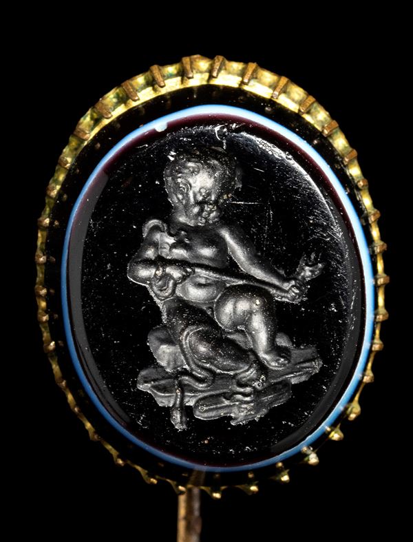 A dark glass paste impression set in a gold stick pin. Hercules as a child killing the snakes